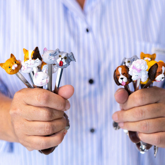 Vrouw houdt Blond Amsterdam theelepels vast, links de set met kattenkopjes en rechts de set met hondenkopjes uit de Dier collectie.