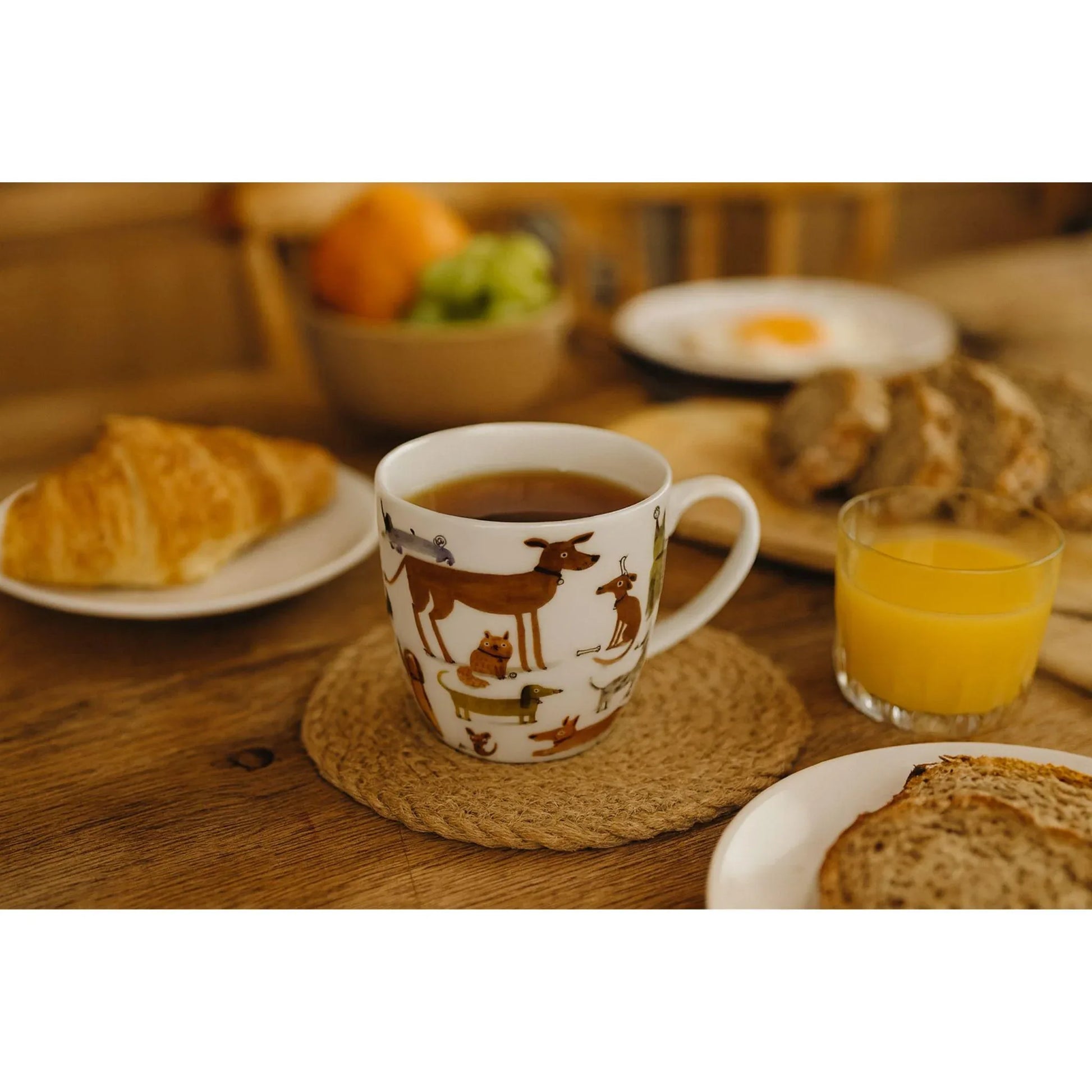 Porseleine mok met hondenillustraties gevuld met thee op een sfeervolle ontbijttafel, perfect voor een warm en ontspannen theemoment.